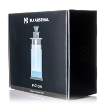 A black box with the MJ Arsenal logo and an illustration of the MJ Arsenal Piston Gravity Bong, a borosilicate glass gravity water pipe, features its product name and description on a reflective surface.