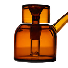 A close-up of the NWTN Home Vesper Bubbler, made from amber-hued borosilicate glass with a cylindrical form and a slim side spout, shown against a white background.