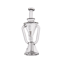 The MJ Arsenal Time Turner Mini Dab Rig is a clear, intricately designed borosilicate glass piece with a geometric hourglass shape, two side handles, and a round stopper, shown empty against a white background.