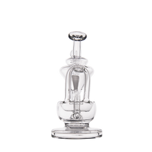 The MJ Arsenal Claude Mini Dab Rig is a clear glass recycler rig with an intricate design, multiple curved tubes, and a wide base, photographed against a plain white background.