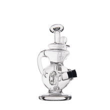 The MJ Arsenal Mini Jig Mini Dab Rig features a clear, intricately designed body with a cylindrical neck, round base, and side-mounted black bowl, shown against a plain white background.