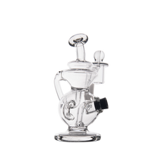The MJ Arsenal Mini Jig Mini Dab Rig features clear glass, a round base, multiple curved chambers, and an angled mouthpiece, shown against a plain white background.