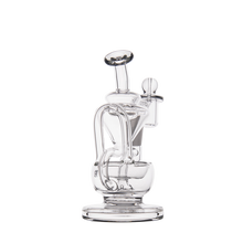 The MJ Arsenal Claude Mini Dab Rig is a clear glass recycler with a unique artistic design, featuring curved tubes and a round base, shown upright against a white background.