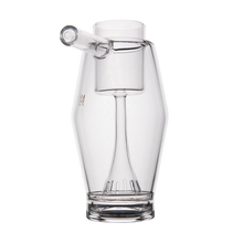 The MJ Arsenal Proxy Bubbler is a clear borosilicate glass vessel with a cylindrical chamber, angled spout, and a slotted diffuser stem—making it an ideal dabbing accessory, shown on a plain white background.