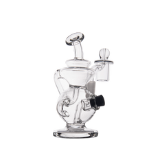 The MJ Arsenal Mini Jig Mini Dab Rig, featuring clear glass, a round base, curved neck, multiple chambers, and a side attachment, is shown against a plain white background.