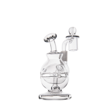 The MJ Arsenal Royale Mini Dab Rig is a clear borosilicate glass piece with a round base, curved neck, and attached quartz banger. It includes a matching glass carb cap, all photographed against a white background.