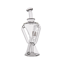 The MJ Arsenal Time Turner Mini Dab Rig is a clear borosilicate glass piece featuring an hourglass-shaped base, angled neck, and curved arms, shown isolated on a white background.