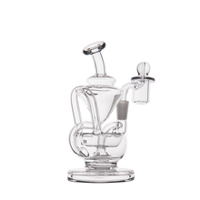 The MJ Arsenal Claude Mini Dab Rig is a clear glass recycler with a cylindrical base, curved neck, and attached bowl. It features looping tubes and a side chamber for smooth hits, perfect for smoking or vaporizing.