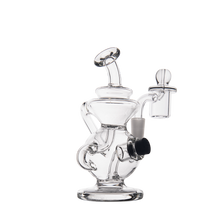 The MJ Arsenal Mini Jig Mini Dab Rig is a clear glass piece featuring a curved mouthpiece, cylindrical base, and intricate tubing. It includes a detachable bowl and side percolator chamber, photographed on a plain white background.