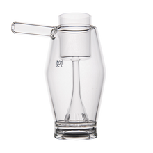 The MJ Arsenal Proxy Bubbler is a clear borosilicate glass pitcher with a cylindrical side handle and unique inner chamber, featuring a funnel-like structure—displayed on white and ideal as a stylish dabbing accessory.