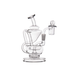 The MJ Arsenal Claude Mini Dab Rig is a clear glass rig with artistic curves, chambers, a bent mouthpiece, flat circular base, and side-attached glass bowl. Shown on a plain white background.