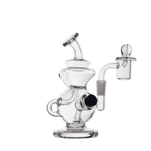 The MJ Arsenal Mini Jig Mini Dab Rig features clear glass with a curvy design, dome-shaped base, angled mouthpiece, side handle, built-in storage jar, and attached banger with carb cap—all shown on a white background.