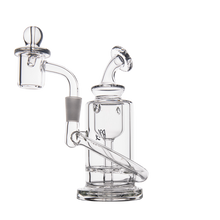 The MJ Arsenal Ursa Mini Dab Rig, made of clear borosilicate glass with a cylindrical chamber, angled mouthpiece, side arm, and a banger topped with a marble carb cap, is displayed against a plain white background.