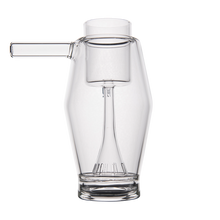 The MJ Arsenal Proxy Bubbler, made of clear borosilicate glass, features a left cylindrical spout and an inner chamber with vertical slits at the base, shown here against a white background.
