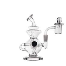 The MJ Arsenal Mini Jig Mini Dab Rig is a clear glass water pipe with a round base, side handle, curved mouthpiece, attached bowl, and built-in storage jar—ideal for concentrate fans. Displayed on a white background.