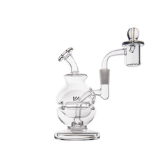 The MJ Arsenal Royale Mini Dab Rig, made of durable borosilicate glass, features a round base, angled mouthpiece, and an attached banger with carb cap on the right side. It appears empty and is set against a plain white background.