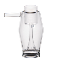 The MJ Arsenal Proxy Bubbler is a clear borosilicate glass piece with a modern design, featuring a left-side cylindrical spout and an inner chamber with vertical slits at the bottom, displayed against a plain white background.