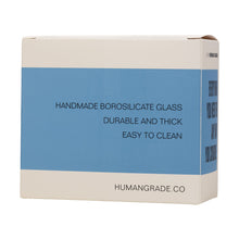 A white box with a blue label reads "Frit Hammer Bubbler—handmade borosilicate glass, durable and thick, double percolator design, easy to clean." The website humangrade.co is printed at the bottom.