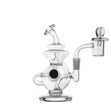 The MJ Arsenal Mini Jig Mini Dab Rig is a clear glass rig with a round base, side handle, bent mouthpiece, quartz banger, and built-in storage jar—displayed against a plain white background.