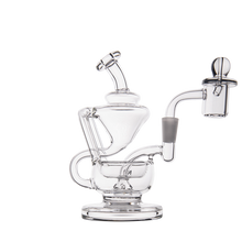 The MJ Arsenal Claude Mini Dab Rig features clear glass, a round base, angled neck, attached bowl, intricate glasswork, and a domed carb cap. Displayed against a white background.