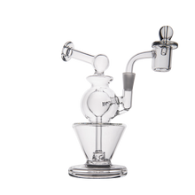 The MJ Arsenal Gemini Mini Dab Rig is a clear borosilicate glass water pipe with a round chamber, angled mouthpiece, and side attachment, designed for compact portability. Displayed against a white background.