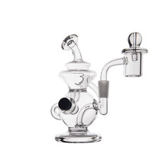 The MJ Arsenal Mini Jig Mini Dab Rig is a clear glass recycler with a wide base, curved neck, side-mounted chamber, and built-in storage jar, shown isolated on a white background.