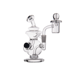 The MJ Arsenal Mini Jig Mini Dab Rig is a clear dab rig with a curved mouthpiece, side arm, cylindrical chamber, and built-in storage jar for concentrates. Perfect for vaporizing on the go. Shown isolated on a white background.