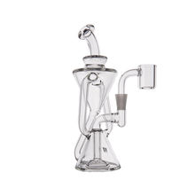 The MJ Arsenal Time Turner Mini Dab Rig is a clear borosilicate glass rig with a unique angled design, multiple chambers, bent neck mouthpiece, and side-mounted bowl. This compact piece is showcased against a plain white background.