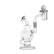 The MJ Arsenal Atlas Mini Dab Rig is a clear borosilicate glass rig with a round chamber, side handle, and attached quartz banger with bubble carb cap, shown compactly against a plain white background.