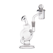 The MJ Arsenal Atlas Mini Dab Rig, crafted from clear borosilicate glass, has a round chamber, bent neck, side mouthpiece, and an attached banger for vaporizing concentrates. Shown on a plain white background.