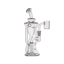 The MJ Arsenal Time Turner Mini Dab Rig is a clear borosilicate glass piece featuring a spiral chamber, angled mouthpiece, side bowl attachment, and a wide sturdy base for upright stability.