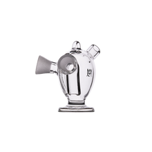 The MJ Arsenal Dubbler Original Double Bubbler features clear borosilicate glass, a rounded body, wide base, angled mouthpiece, side bowl for smooth filtration, and a black logo on the front against a white background.