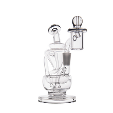 The MJ Arsenal Claude Mini Dab Rig is a clear glass recycler with a complex, multi-chambered design, angled tubes, and a cylindrical mouthpiece, shown against a plain white background.