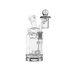 The MJ Arsenal Turbine Mini Dab Rig is a clear borosilicate glass water pipe with a round base, angled mouthpiece, and detachable bowl, designed for vaporizing concentrates, shown against a white background.