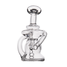 The MJ Arsenal Hydra Vape Edition is a clear glass mini dab rig with a rounded base, angled neck, and circular mouthpiece. It features intricate glasswork, a curved side tube, sturdy build, and splash-resistant bubbler design for concentrates.