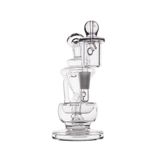 The MJ Arsenal Claude Mini Dab Rig is a clear glass piece with an artistic design featuring multiple chambers and curved sections, shown against a plain white background.