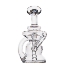 The MJ Arsenal Hydra Vape Edition is a clear glass mini dab rig with a round base, side handle, and upward-facing mouthpiece. Its sculptural design includes a splash-resistant bubbler for smoother concentrate vaporization.