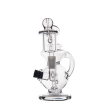 The MJ Arsenal Mini Jig Mini Dab Rig is a clear glass recycler with a round base, side handle, multiple chambers, and built-in storage jar. Perfect for dabbing and vaporizing, it's shown on a plain white background.