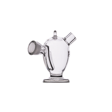 The MJ Arsenal Dubbler Original Double Bubbler, made of clear borosilicate glass and featuring a round body, flat base, short angled spout, and handle-like side protrusion, is shown against a plain white background.
