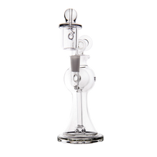 The MJ Arsenal Apollo Mini Dab Rig is a clear borosilicate glass water pipe with a round base, central chamber, vertical neck, and glass bowl attachment, designed for excellent flavor preservation against a plain white background.