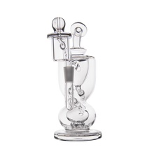The MJ Arsenal Titan Mini Dab Rig, made of clear borosilicate glass with intricate curves and chambers, showcases a cylindrical base, round accents, and a vertical mouthpiece. Photographed against a white background.