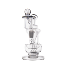 The MJ Arsenal Claude Mini Dab Rig is a clear glass water pipe with a cylindrical chamber, vertical mouthpiece, and bowl attachment, shown against a plain white background.