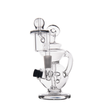 The MJ Arsenal Mini Jig Mini Dab Rig is a clear glass rig featuring intricate curves, a side handle, cylindrical mouthpiece, and removable front bowl, displayed against a plain white background.