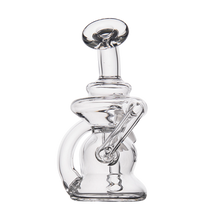 The MJ Arsenal Hydra Vape Edition is a clear glass mini dab rig featuring a cylindrical mouthpiece, angled downstem, and compact intricate design with splash-resistant bubbler functions—displayed on a plain white background.
