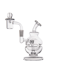 The MJ Arsenal Royale Mini Dab Rig is made of clear borosilicate glass with a rounded base, fab egg percolator, angled mouthpiece, and side chamber. The main chamber displays an overlapping M and J logo. Shown against a plain white background.