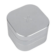 The PAX Herb Grinder is a silver, square aluminum grinder with rounded corners, a minimalist design, a four-petaled flower logo engraved on the lid, and a secure magnetic closure.