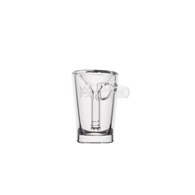 The MJ Arsenal Basin Bubbler is a clear borosilicate glass cup with an inner chamber shaped like a key and a small side handle. Inspired by mini bubbler water filtration, it offers a modern, artistic look against a white background.
