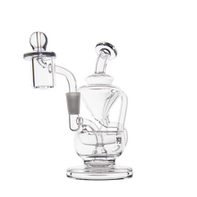 The MJ Arsenal Claude Mini Dab Rig is a clear glass dab rig with a cylindrical chamber, angled mouthpiece, and attached quartz banger, ideal for vaporizing concentrates, shown on a plain white background.