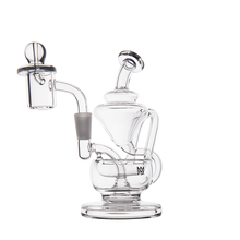 The MJ Arsenal Claude Mini Dab Rig is a clear glass rig with a round base, curved neck, intricate tubing, attached banger, and removable carb cap, displayed on a plain white background.