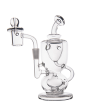 The MJ Arsenal Titan Mini Dab Rig is a clear borosilicate glass rig with a rounded base, angled mouthpiece, attached handle, and side percolator chamber for concentrates. It stands on a flat circular base against a white background.